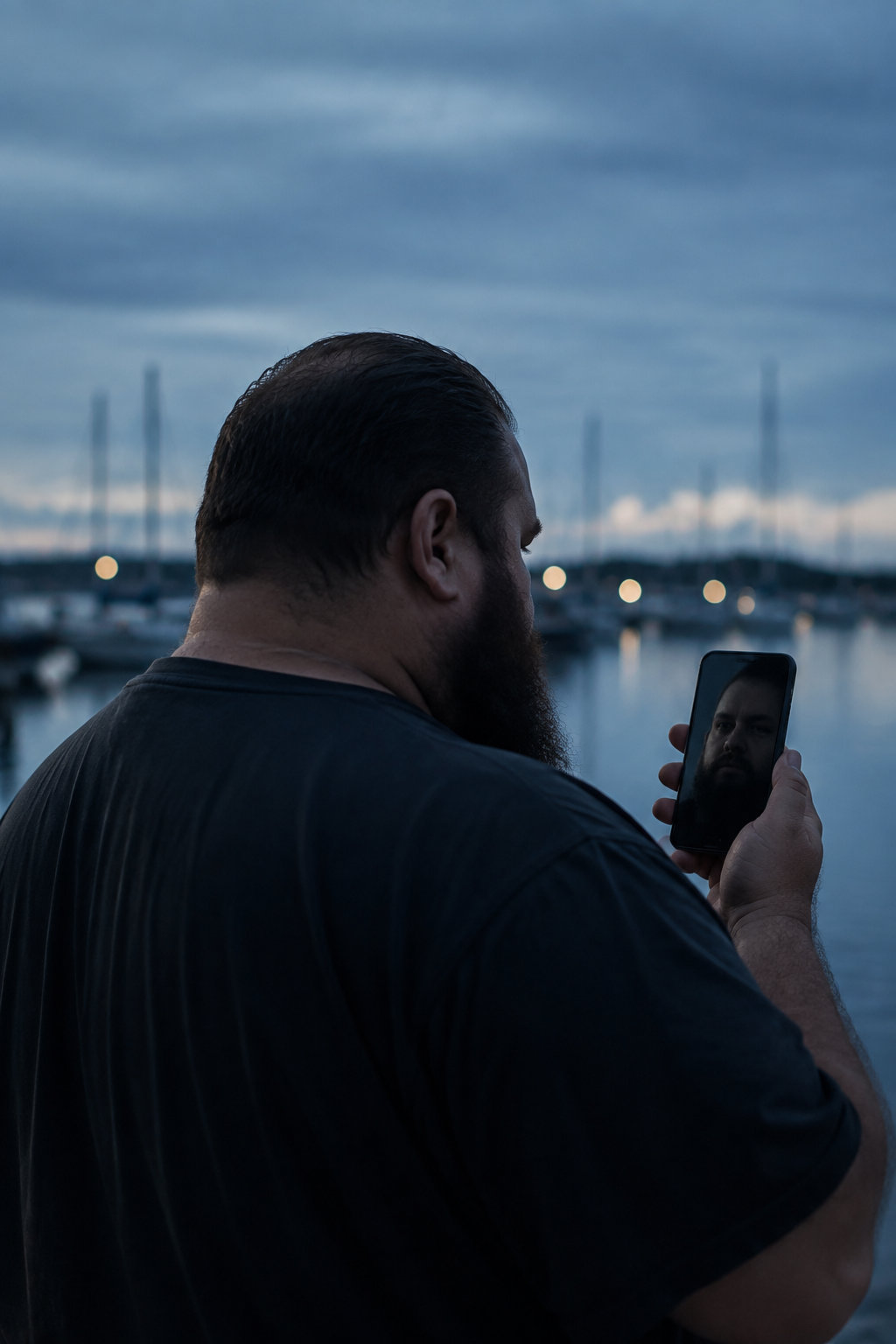 An imaginary man looks at his reflection in a smartphone at a marina at dusk